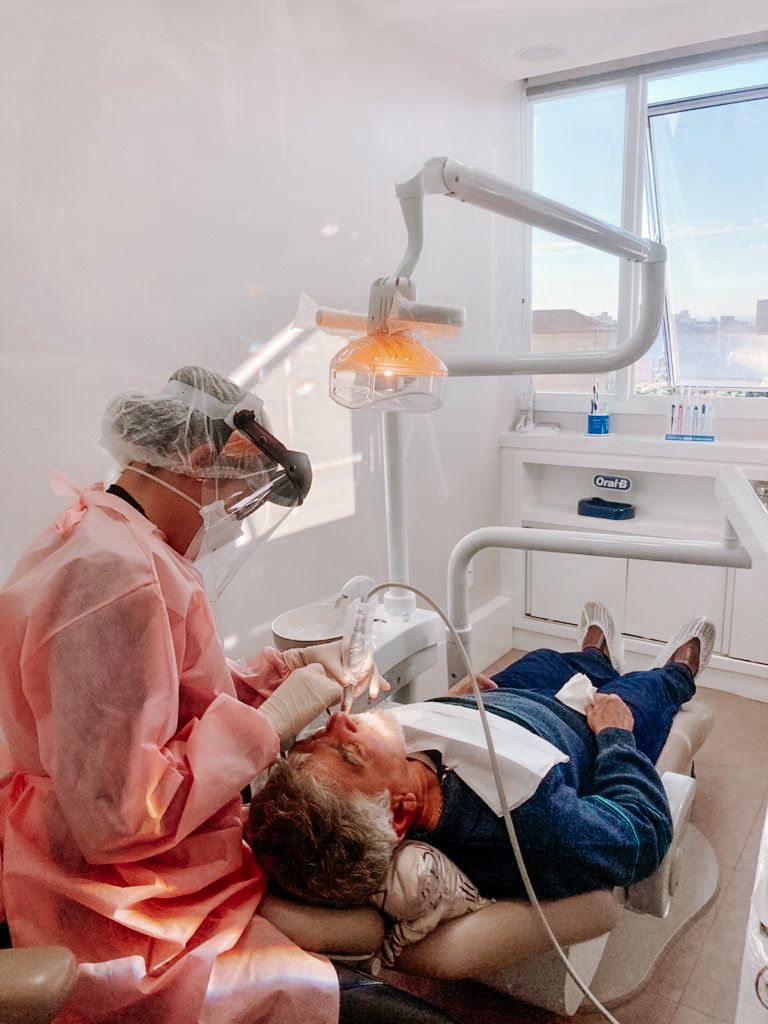 Dra. Thaise atendendo um paciente no consultório, com luz natural da janela